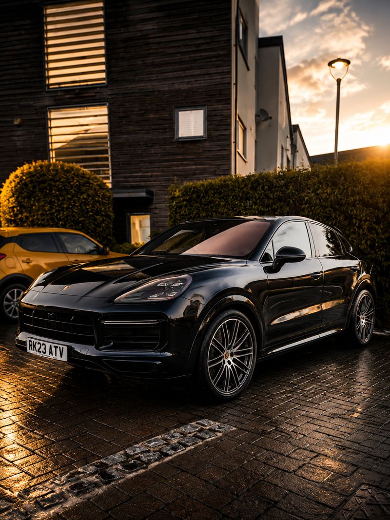 Black Porsche Cayenne Coupe front three-quarter view on wet pavement